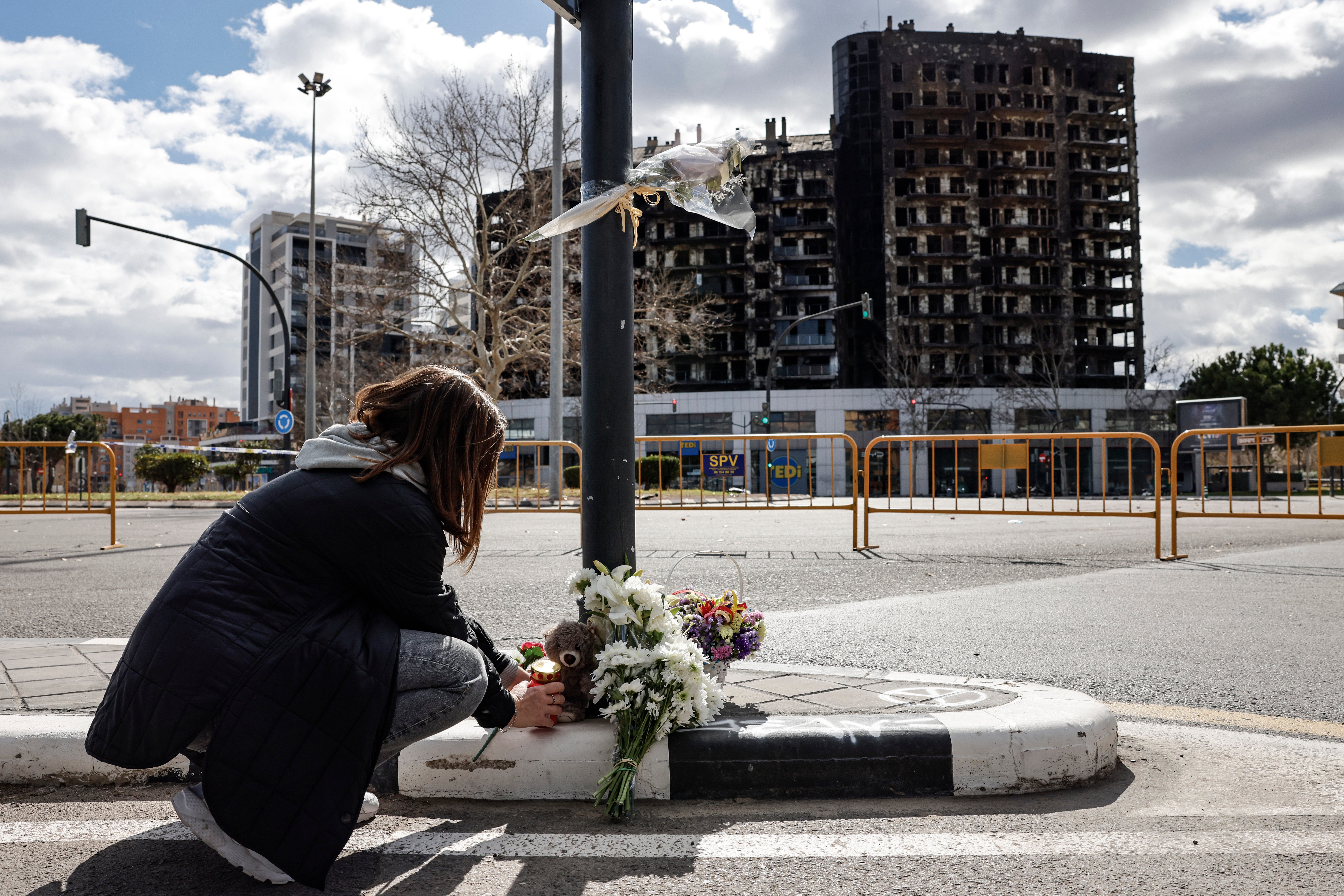 Una niña deposita flores ante la estructura de hormigón del edificio siniestrado en Campanar.