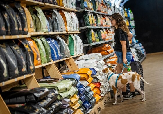 Una joven observa la comida para perros en una tienda especializada junto a su mascota.