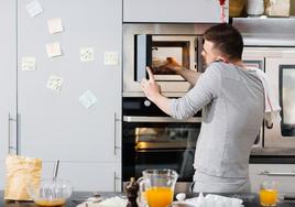 Un hombre cocina en un microondas en una vivienda.