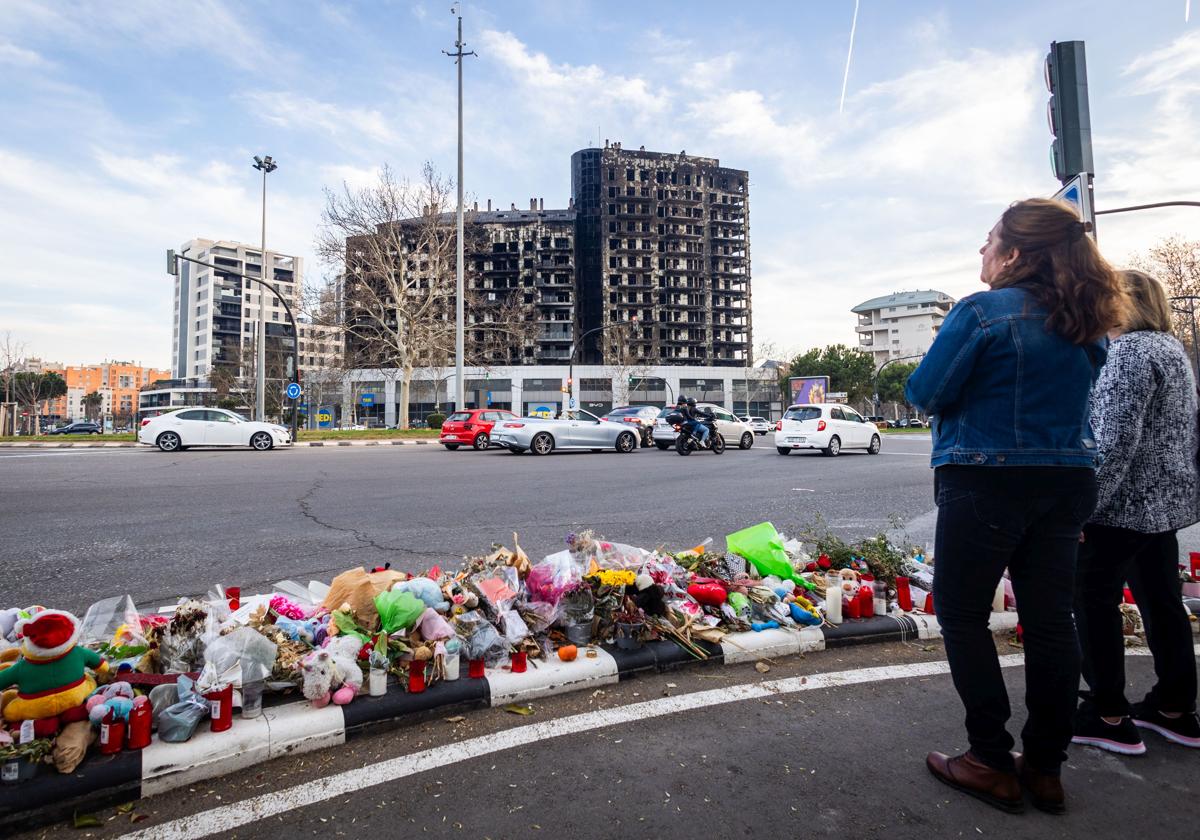 Decenas de velas, muñecos y flores en recuerdo de los fallecidos en el incendio del edificio de Campanar (al fondo).