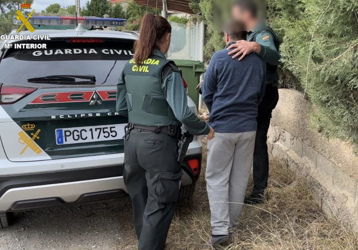 Dos guardias civiles trasladan a uno de los ladrones a un coche patrulla.