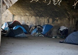 Campamento de personas en situación de sinhogarismo bajo un puente del río.