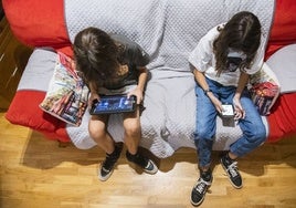 Dos niños con dispositivos digitales en su casa.