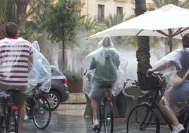 Ciclistas con chubasqueros por el centro de Valencia, bajo la lluvia del pasado 11 de junio en la ciudad.