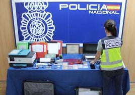 Una agente de la Policía Nacional, junto a los documentos y herramientas confiscados al presunto falsificador.