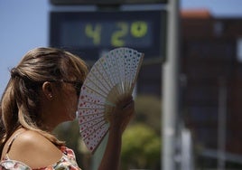 Una mujer se abanica junto a un termómetro de calle que marca 42 grados.