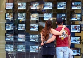 Jovenes mirando escaparates de agencias inmobiliarias.