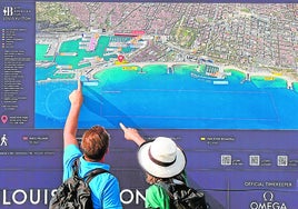 Dos turistas observan las explicaciones del trazado de las regatas en la fan zone de la Barceloneta.