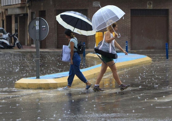 Dos personas cruzan una calle bajo la lluvia.