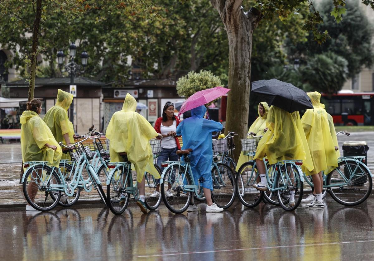 Un grupo de turistas en bicicleta cubiertos con chubasqueros en la plaza del Ayuntamiento.