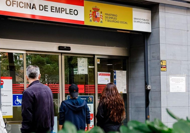 Tres personas esperan a la puerta de una oficina de empleo.