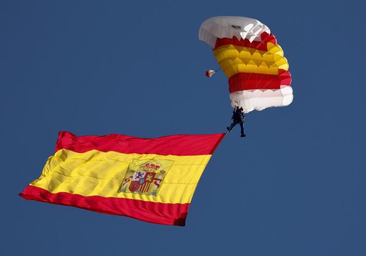 Un paracaidista porta la bandera en un desfile de la Fiesta Nacional.