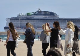 Un grupo de turistas, en la playa, con un crucero de fondo.