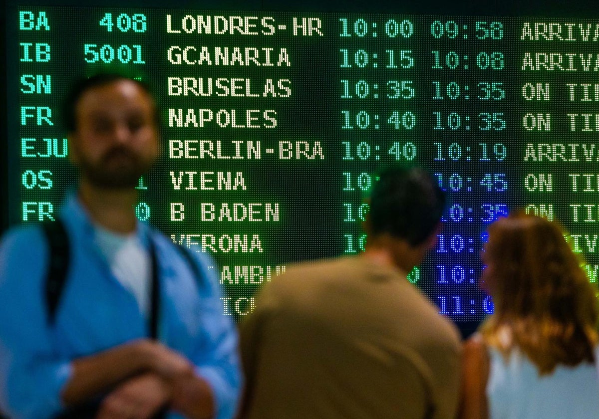 Varios viajeros, delante de una pantalla de llegadas en el aeropuerto de Valencia.