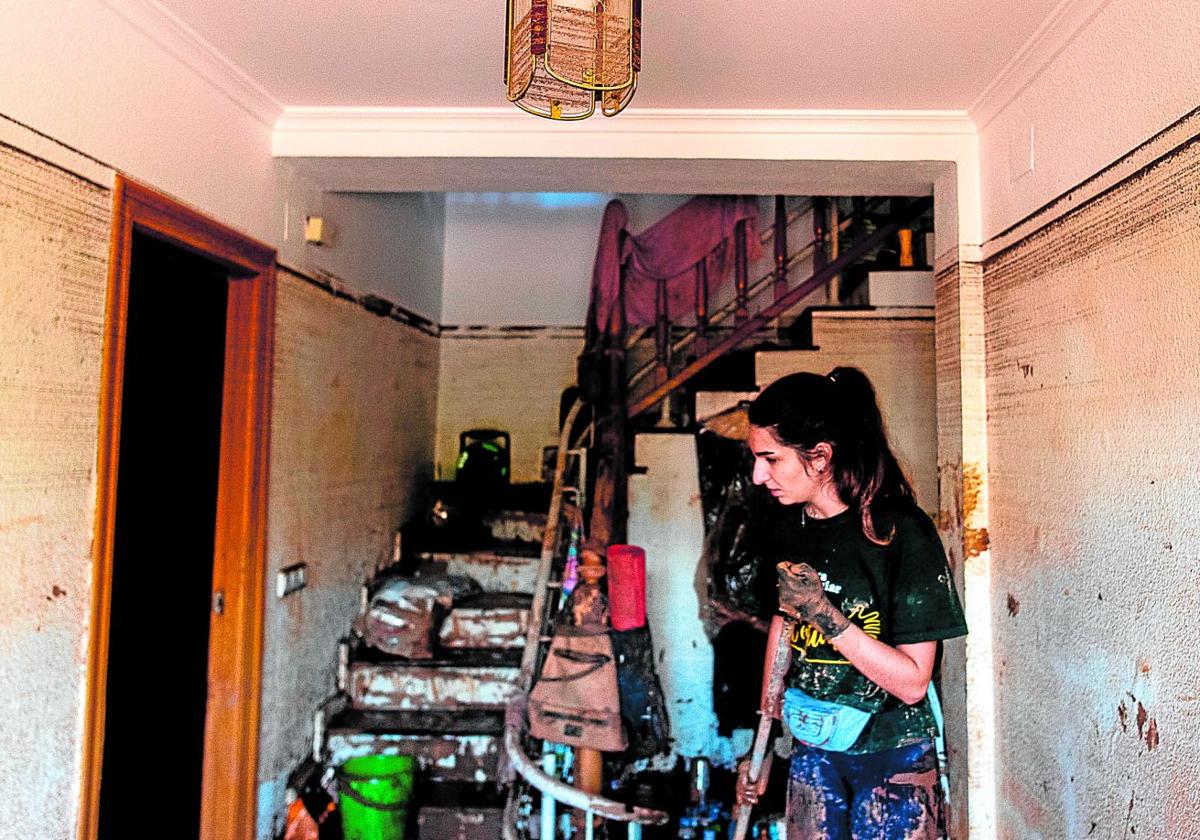 Una mujer quita el barro en una vivienda en la que la lámpara recoge la huella del agua.