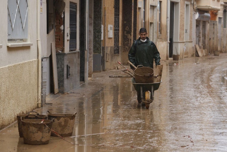 Un vecino traslada en carretilla restos de utensilios para limpiar el barro, bajo la lluvia de este miércoles en Paiporta.