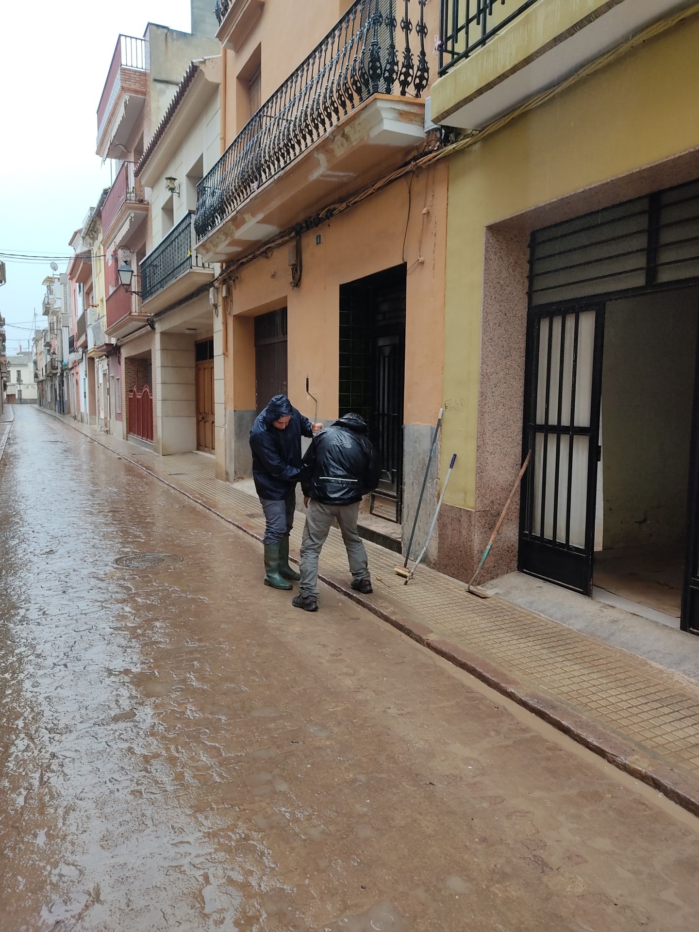 Dos vecinos intentan levantar una alcantarilla llena de barro,