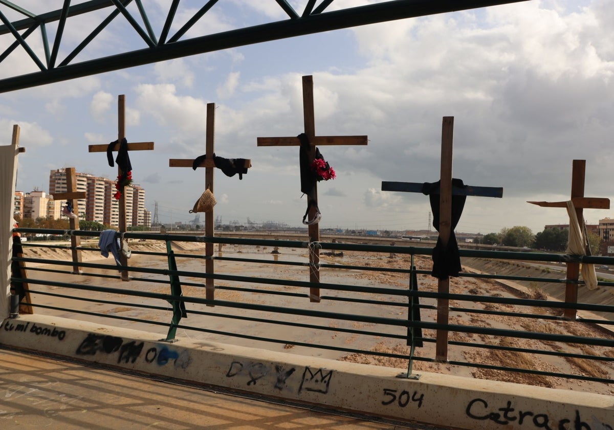 Imagen principal - Cruces decoradas con ropa, botas y un peluche, en la pasarela que salva el río Turia.