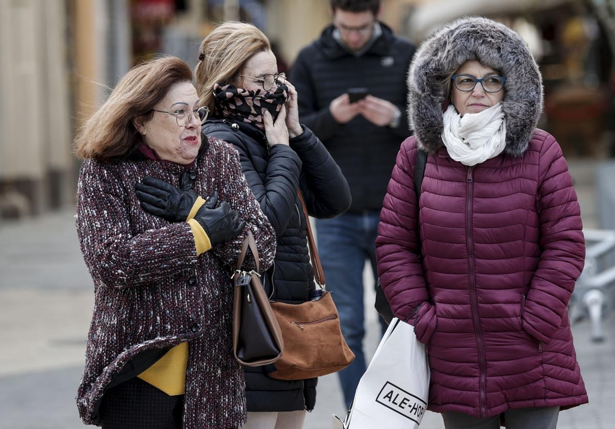 Tres mujeres protegidas contra el viento y el frio pasean por el centro de Valencia.