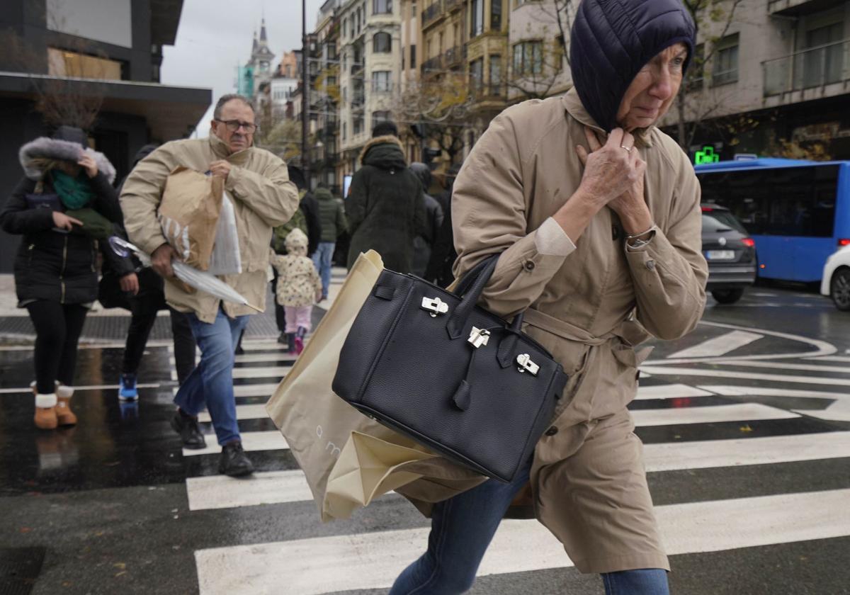 Varias personas cruzan un paso de cebra mientras sopla el fuert viento.