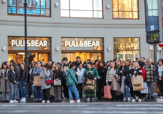 Peatones esperando que el semáforo se ponga en verde, en la calle Colón, con bolsas de compra.