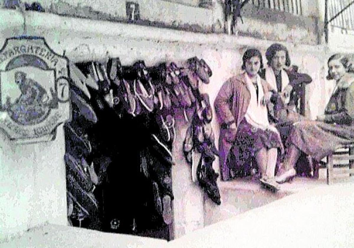 Imagen principal - Año 1925. Tres mujeres sentadas junto a uno de los locales dedicados a alpargatería. | El número 11. El puesto de Nicolás Llavador, donde se acumulan productos para uso doméstico. | Cubos y pozales. Fotografía tomada en los años cincuenta donde se aprecian multitud de artilugios y enseres para la limpieza y las tareas de la casa. 