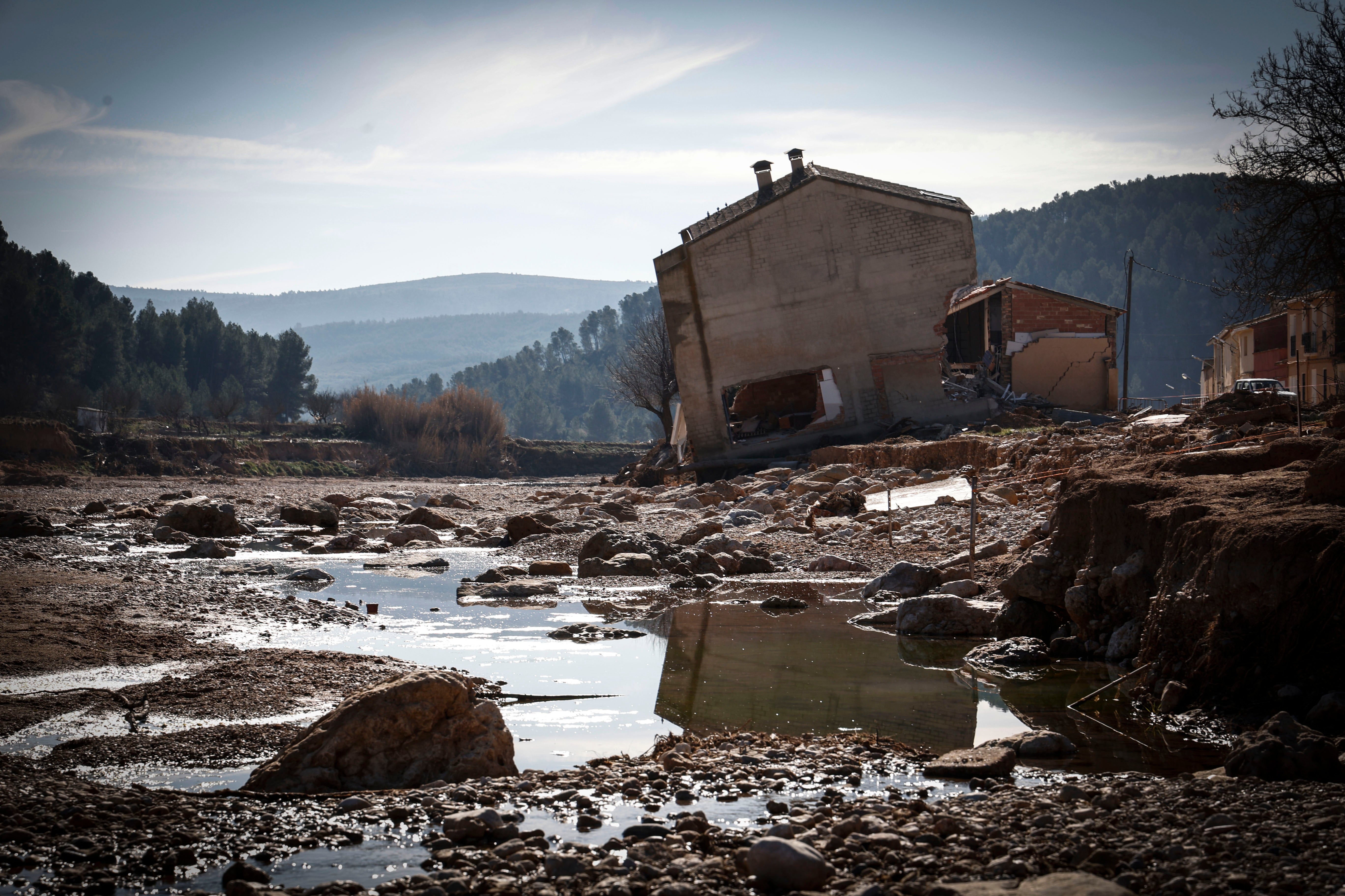 Imagen secundaria 1 - José trabaja en su casa entre el barro y los destrozos. La furia del Magro destrozó el cauce y las casas cercanas de la aldea. La carretera, aún cortada, con obreros reparando el puente derribado.