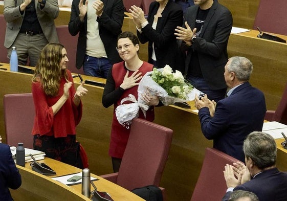 Mas recibe un ramo de flores de sus compañeros de Compromís en Les Corts mientras aplauden en pie los diputados de su grupo, del PSPV, del PP, de Vox y los miembros del Consell.