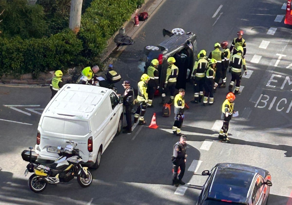 Un grupo numeroso de bomberos y policías locales junto al vehículo volcado.