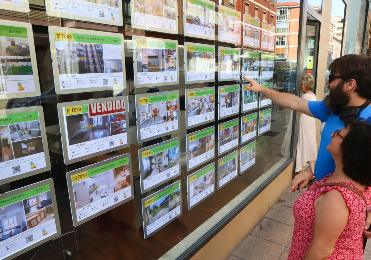 Dos jóvenes miran pisos en el escaparate de una inmobiliaria.
