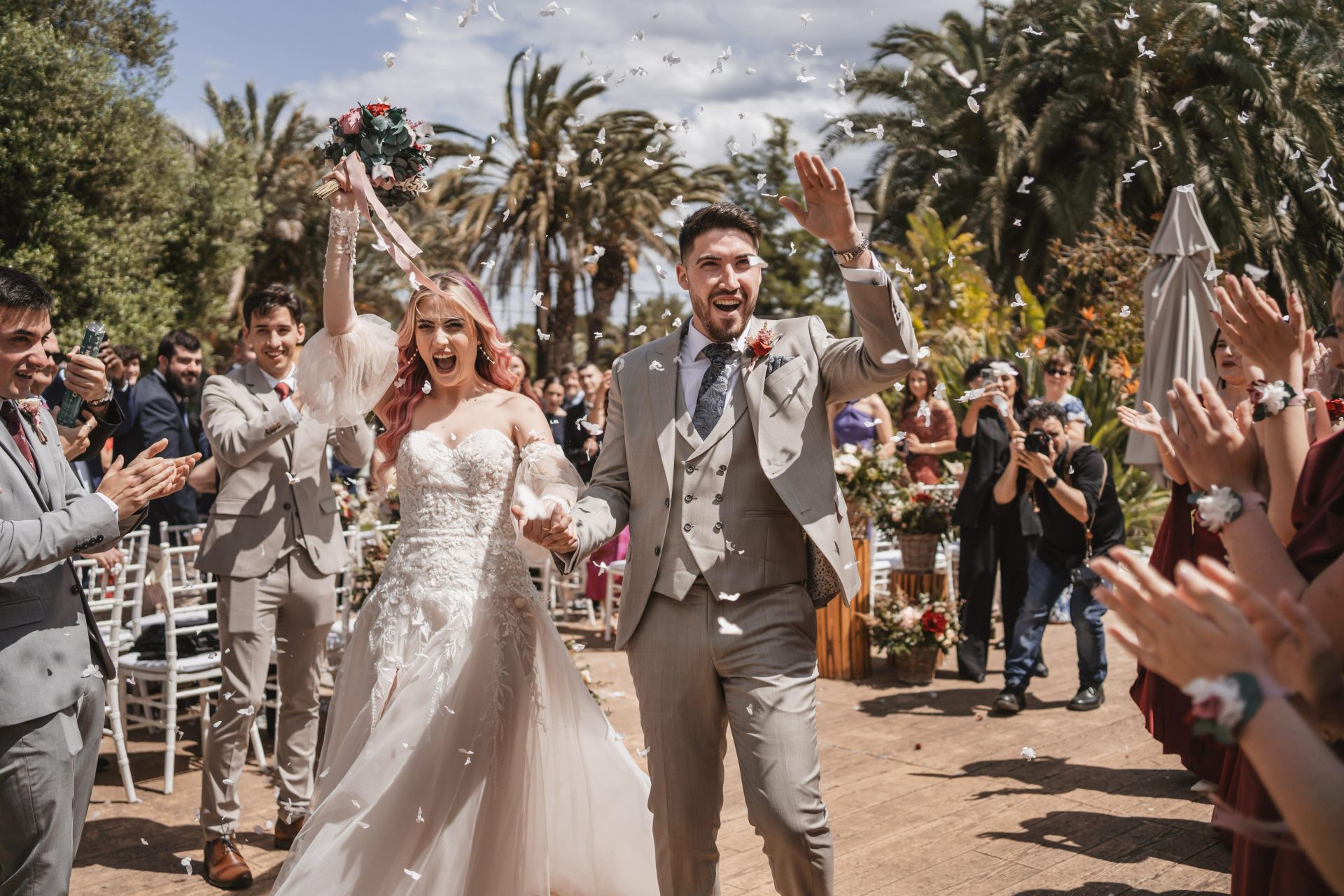 La pareja saluda a los invitados bajo una lluvia de pétalos acabada la ceremonia.