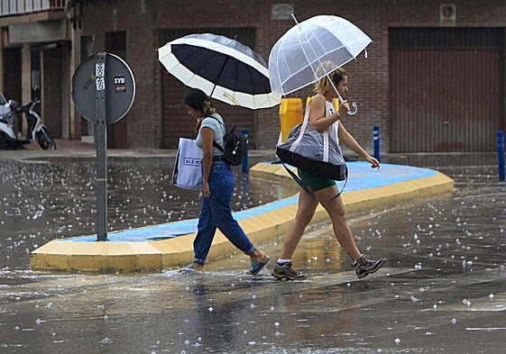 Dos personas cruzan una calle bajo la lluvia.