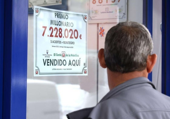 Administración de lotería junto al cartel de un premio millonario.