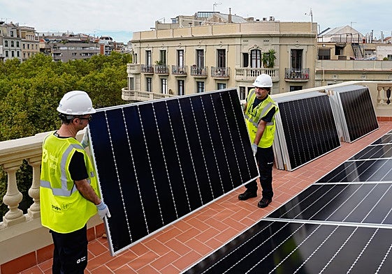 Dos trabajadores colocan una placa solar en la terraza de una vivienda.