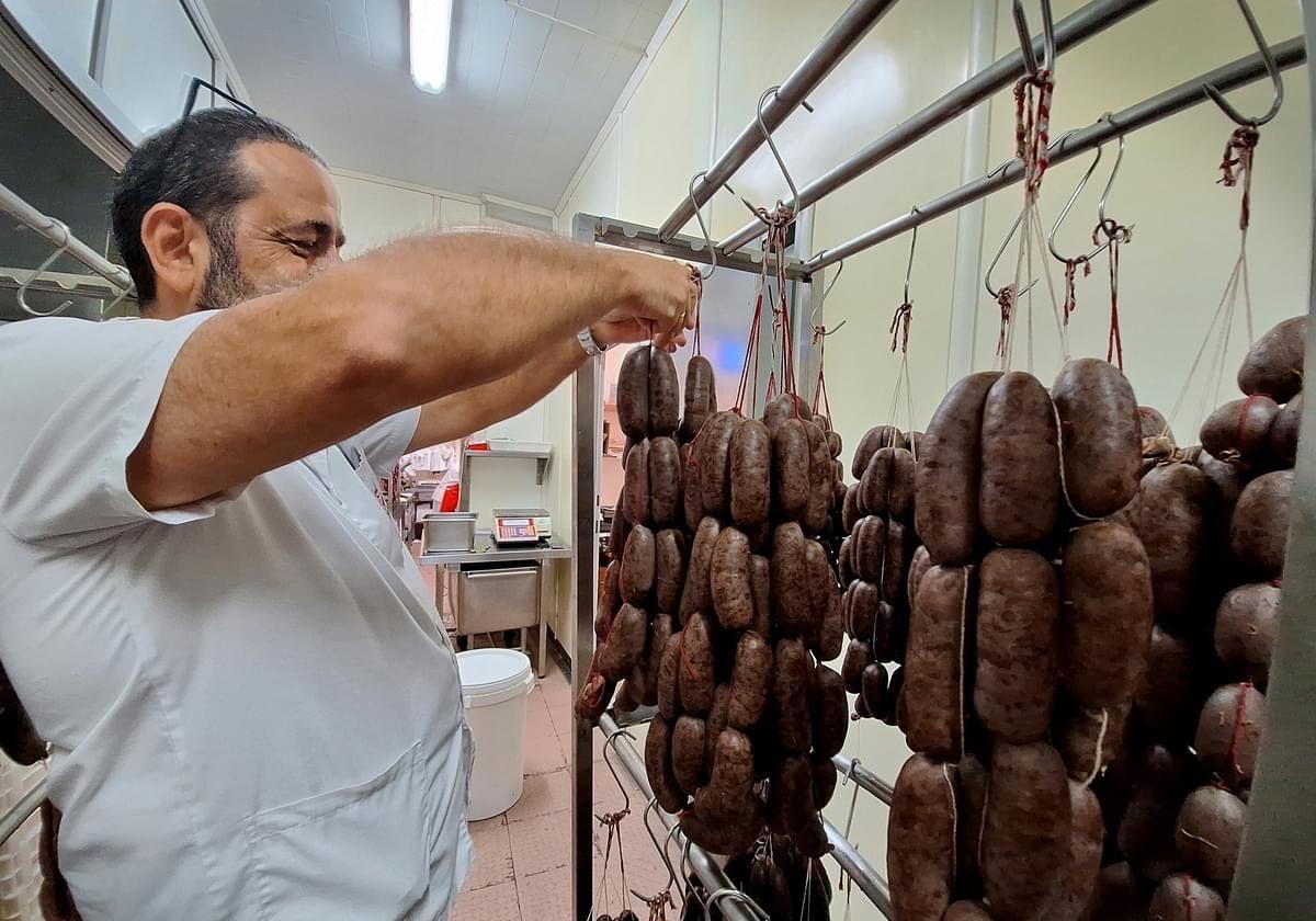 Un carnicero maneja unas ristras de embutido de apetitoso aspecto.