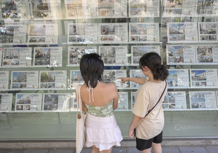 Dos jóvenes miran anuncios de pisos para alquilar en una inmobiliaria.