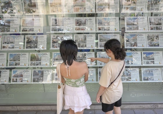 Dos jóvenes miran anuncios de pisos para alquilar en una inmobiliaria.