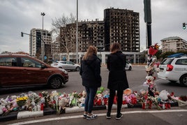 Dos jóvenes, ante el edificio calcinado y las ofrendas florales tras la tragedia.