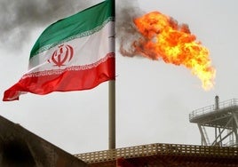 Una llamarada de gas en una plataforma de producción de petróleo en los campos petrolíferos de Soroush se ve junto a una bandera iraní en el Golfo Pérsico.