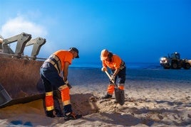 Dos operarios en la playa de Sagunto.