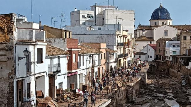 Imagen antes - La imagen es de la mañana siguiente de la dana, con un ejército de voluntarios ayudando a los vecinos de la calle Buñol. Ahora, ocho meses después, se trata de volver a la normalidad con una obra que ha empezado por el alcantarillado y los colectores