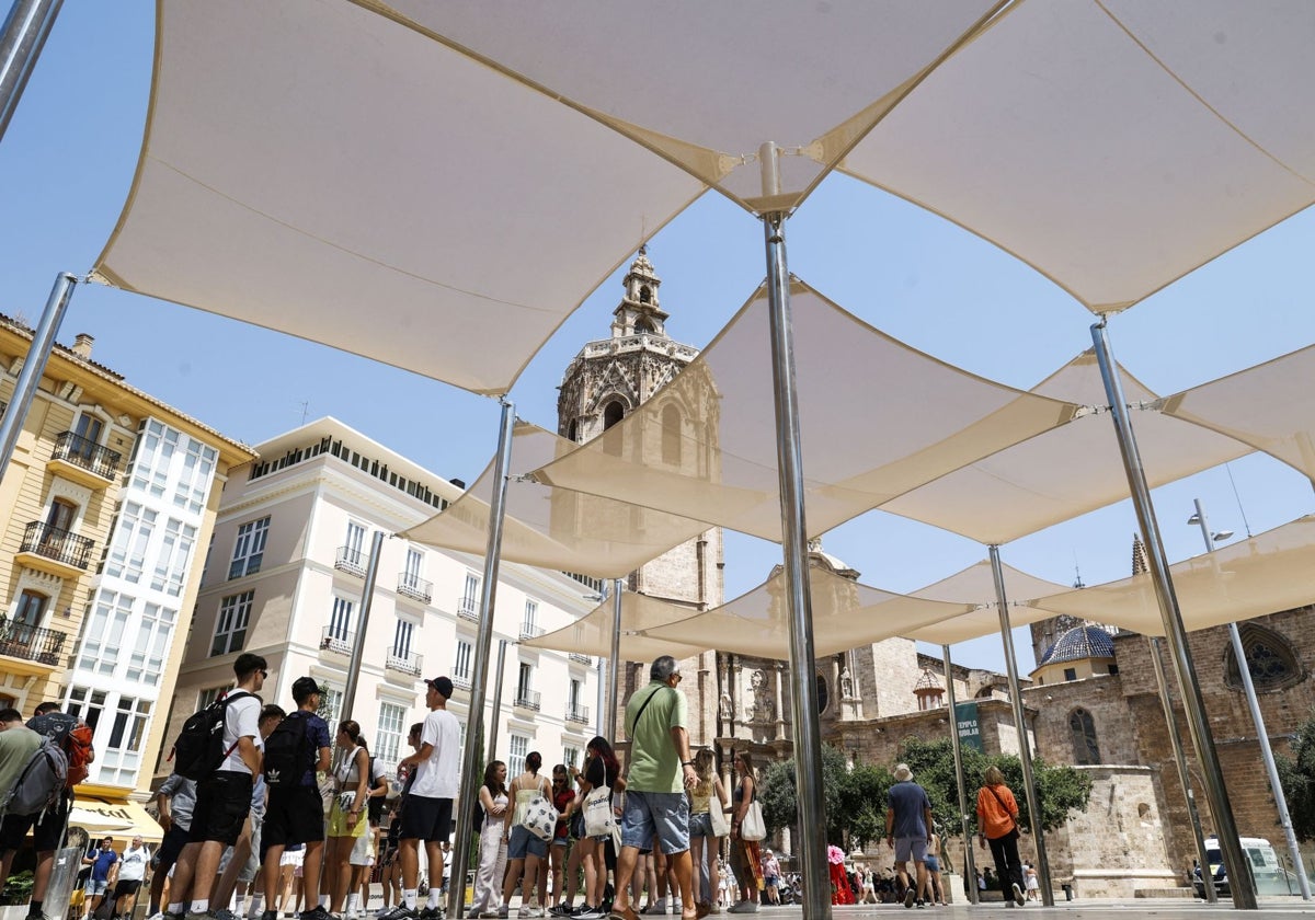 Turistas resguardándose del sol en los toldos de la plaza de la Reina de Valencia.