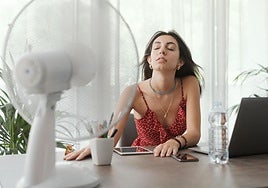 Una mujer intenta refrescarse con un ventilador.
