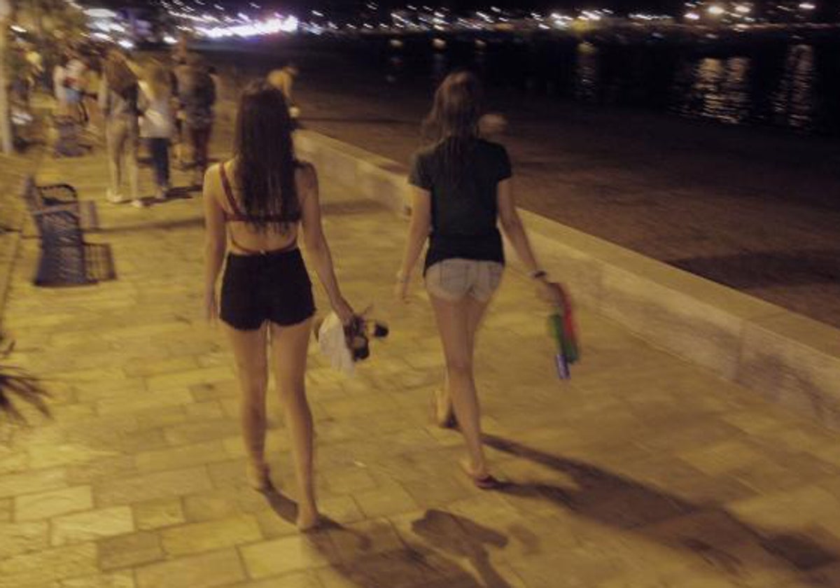 Dos adolescentes caminan de noche por un paseo marítimo.