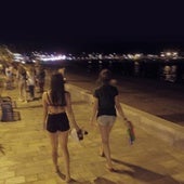 Dos adolescentes caminan de noche por un paseo marítimo.