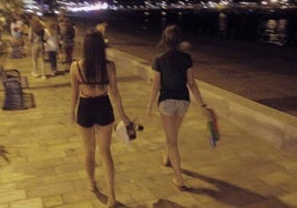 Dos adolescentes caminan de noche por un paseo marítimo.