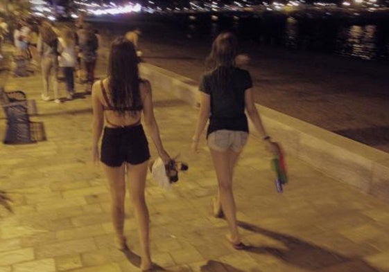 Dos adolescentes caminan de noche por un paseo marítimo.