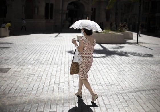 Una mujer se proteje del sol con una sombrilla.