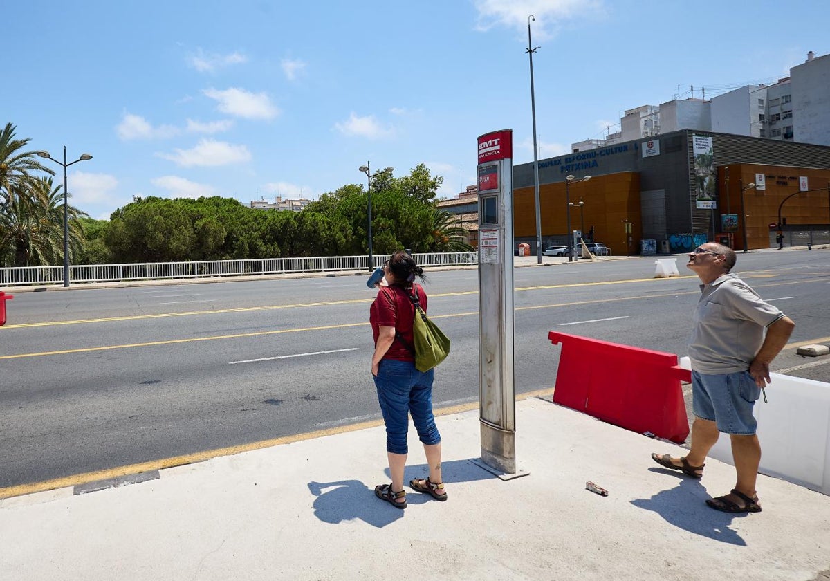 Dos usuarios en la parada de la EMT en medio del puente de Campanar que apenas tiene sombra.