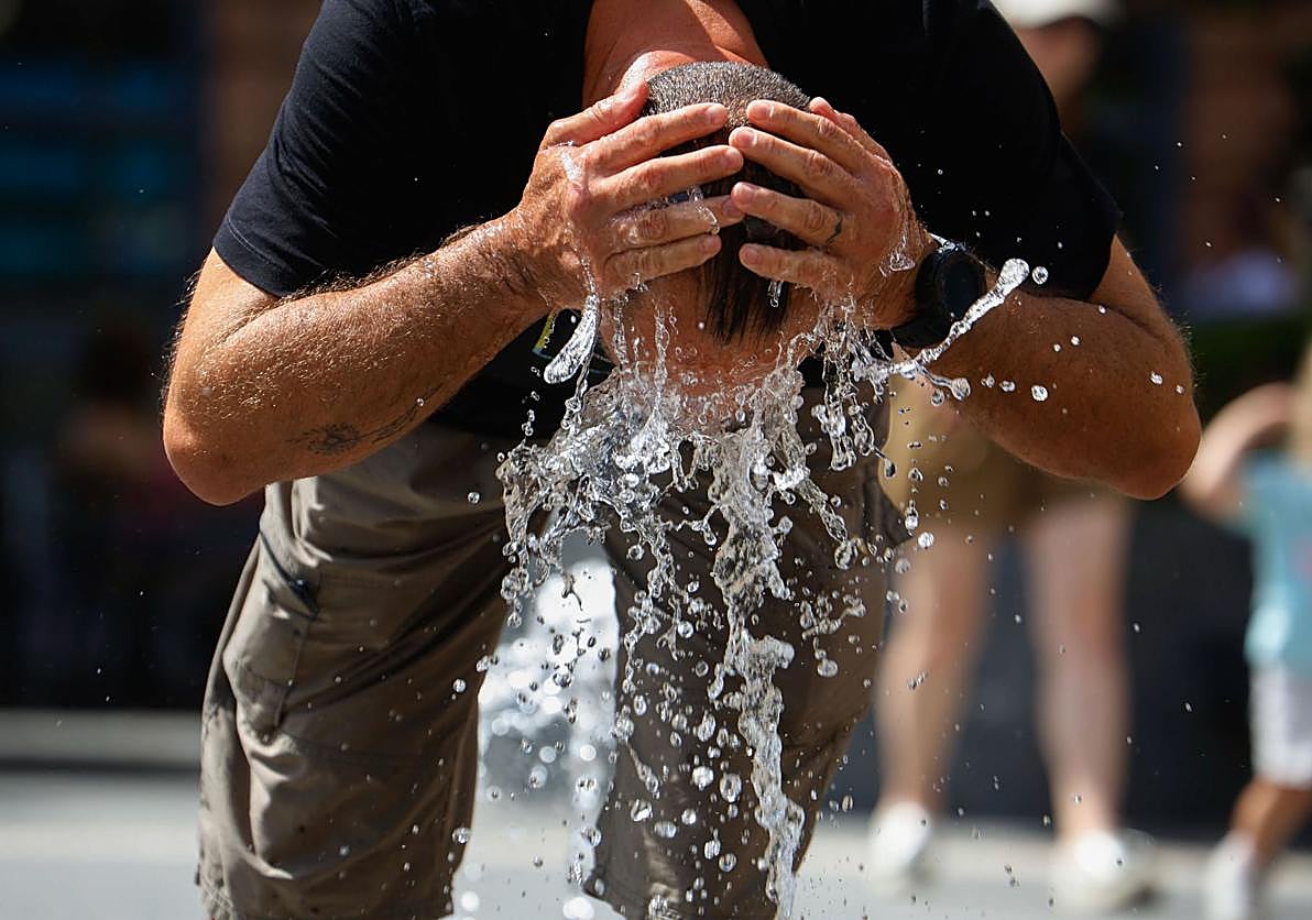 Un hombre refrescándose en una fuente durante una ola de calor.